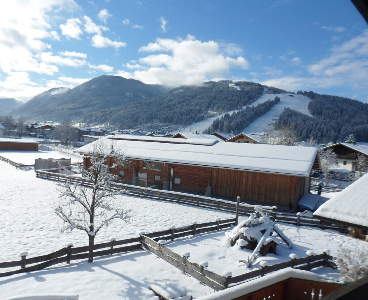 View from the farmhouse of the snowy winter landscape with a ski slope and surrounding buildings.