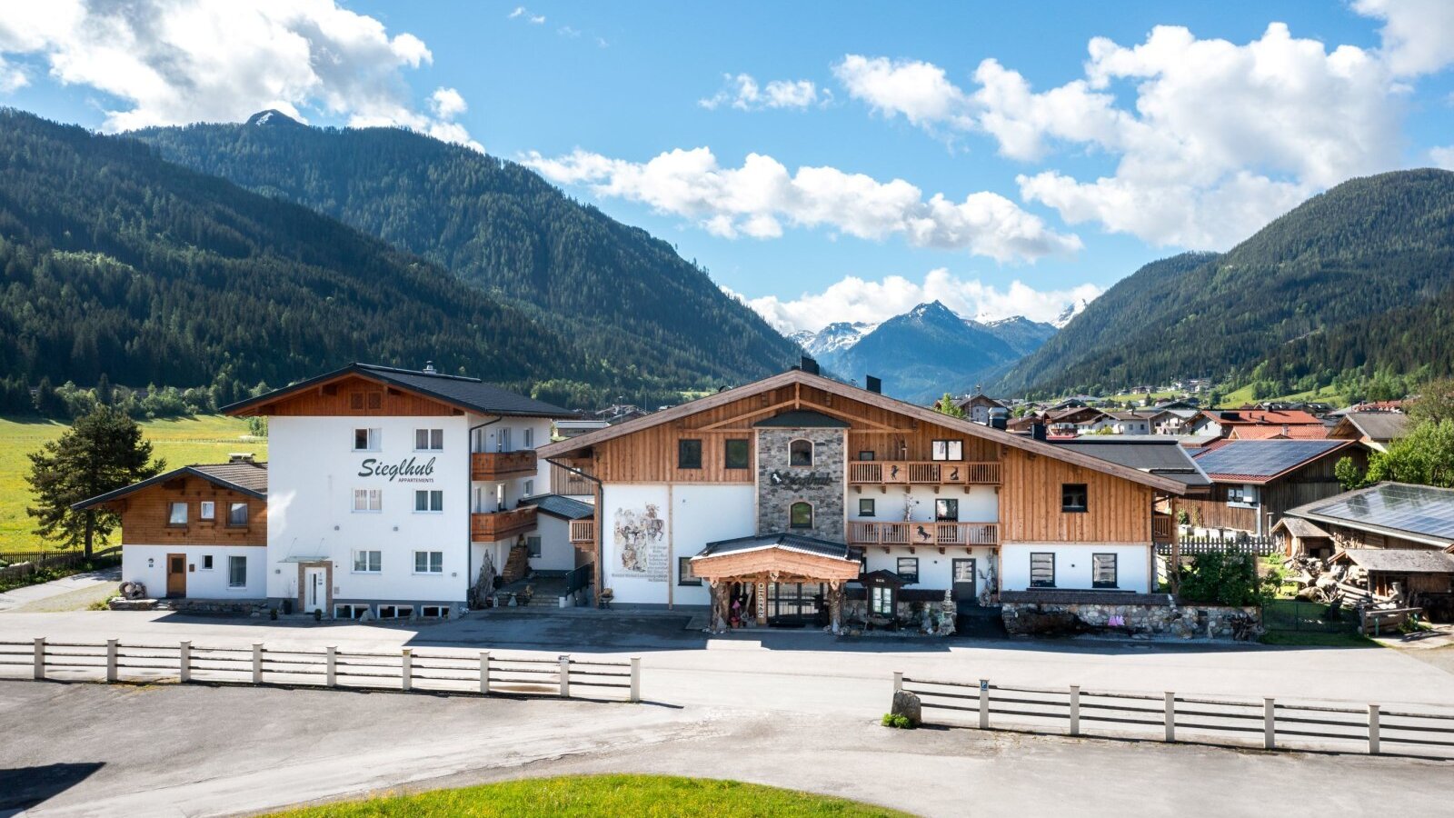 The Siegthub Farm House exterior, featuring traditional architecture with wooden elements and balconies, set against a backdrop of green mountains.