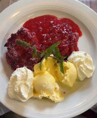 Dessert with berry sauce, vanilla ice cream, whipped cream, and mint garnish, available at the farmhouse.