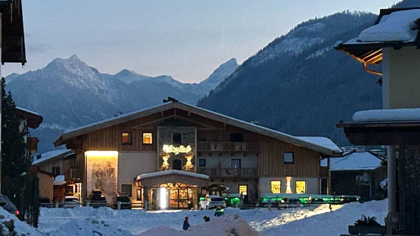 The Bauernhof in winter, featuring an illuminated entrance and snow-covered mountains in the background.