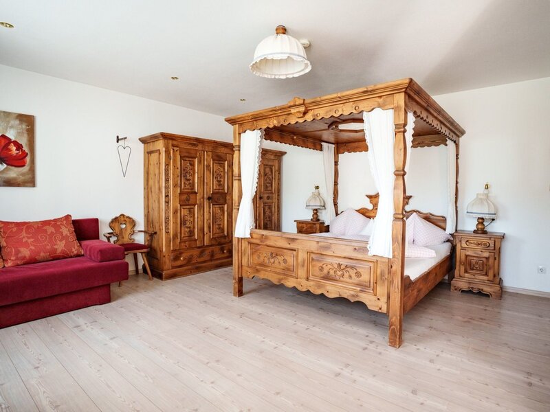 Bedroom in the farmhouse with a four-poster bed, wooden wardrobe, and red sofa.