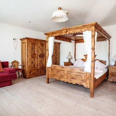 Bedroom in the farmhouse with a four-poster bed, wooden wardrobe, and red sofa.