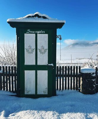 The snow-covered entrance to the farm garden of the farmhouse, featuring a traditional wooden fence.
