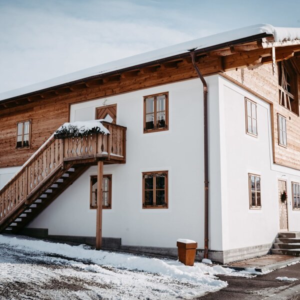 The Farm House exterior in winter, featuring white walls, wooden siding, and an external staircase leading to a balcony.