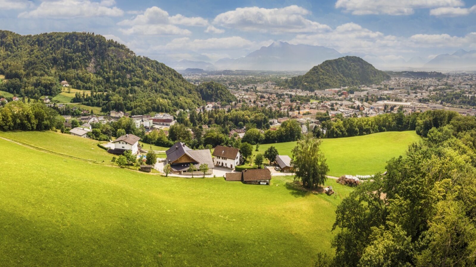 Scenic view of the farmhouse, surrounded by lush green meadows with a panoramic vista of the town and mountains.