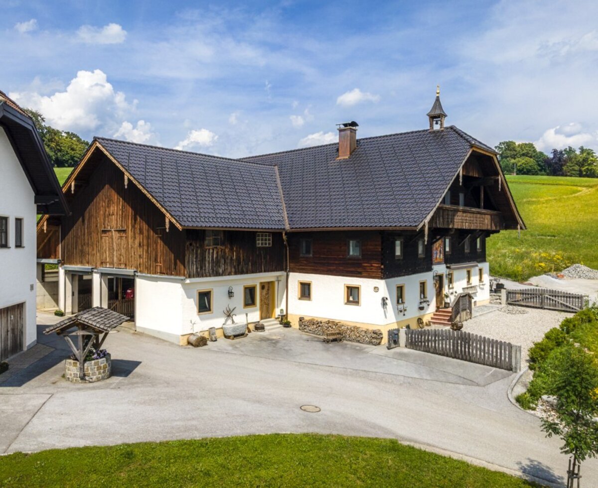 The inviting farmhouse featuring traditional wood and stone architecture, surrounded by green fields under a blue sky.