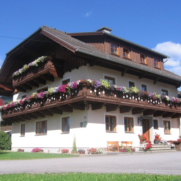 Exterior of the farmhouse with multiple balconies decorated with colorful flower boxes and an entrance area with wooden benches.