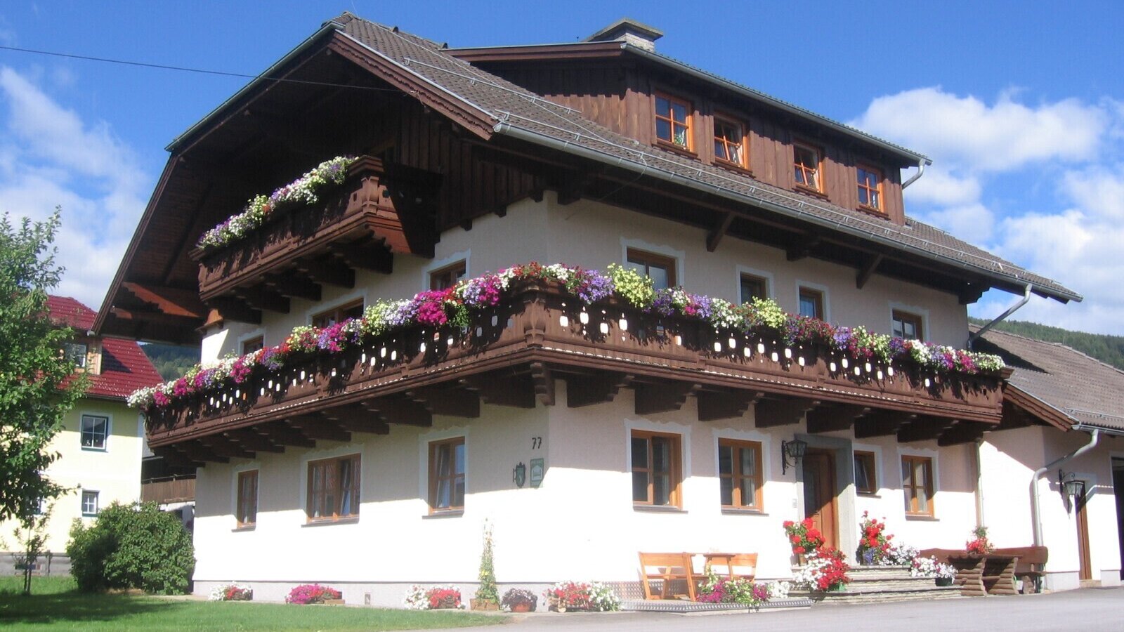 Exterior of the farmhouse with multiple balconies decorated with colorful flower boxes and an entrance area with wooden benches.