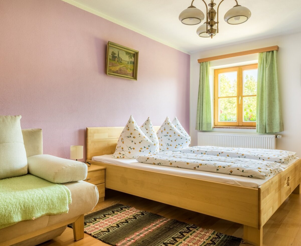 A bedroom in the Farm House apartment, featuring a double wooden bed, a sofa, and wooden flooring.
