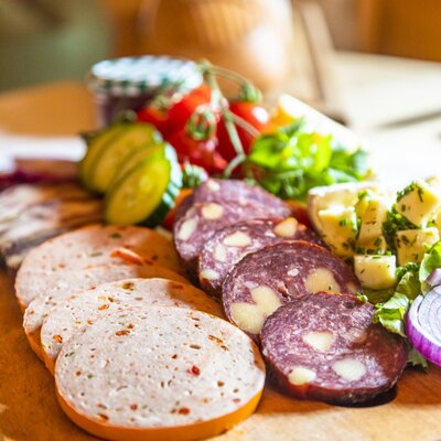A wooden board with sliced sausage, cheese, tomatoes, and cucumber, available for guests at the Farm House.