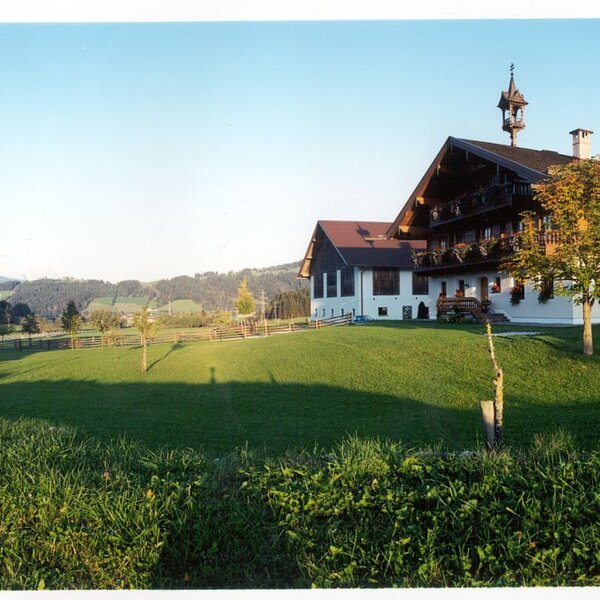 The Farm House exterior with traditional architecture, a bell tower, and surrounding green fields and wooded hills.