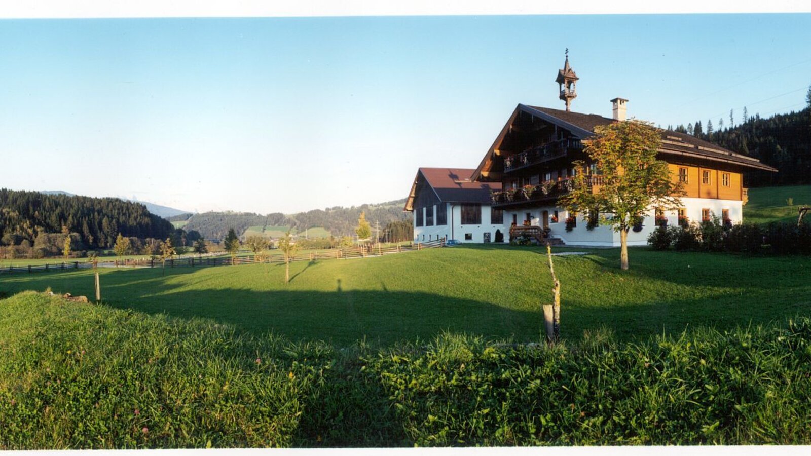 The Farm House exterior with traditional architecture, a bell tower, and surrounding green fields and wooded hills.