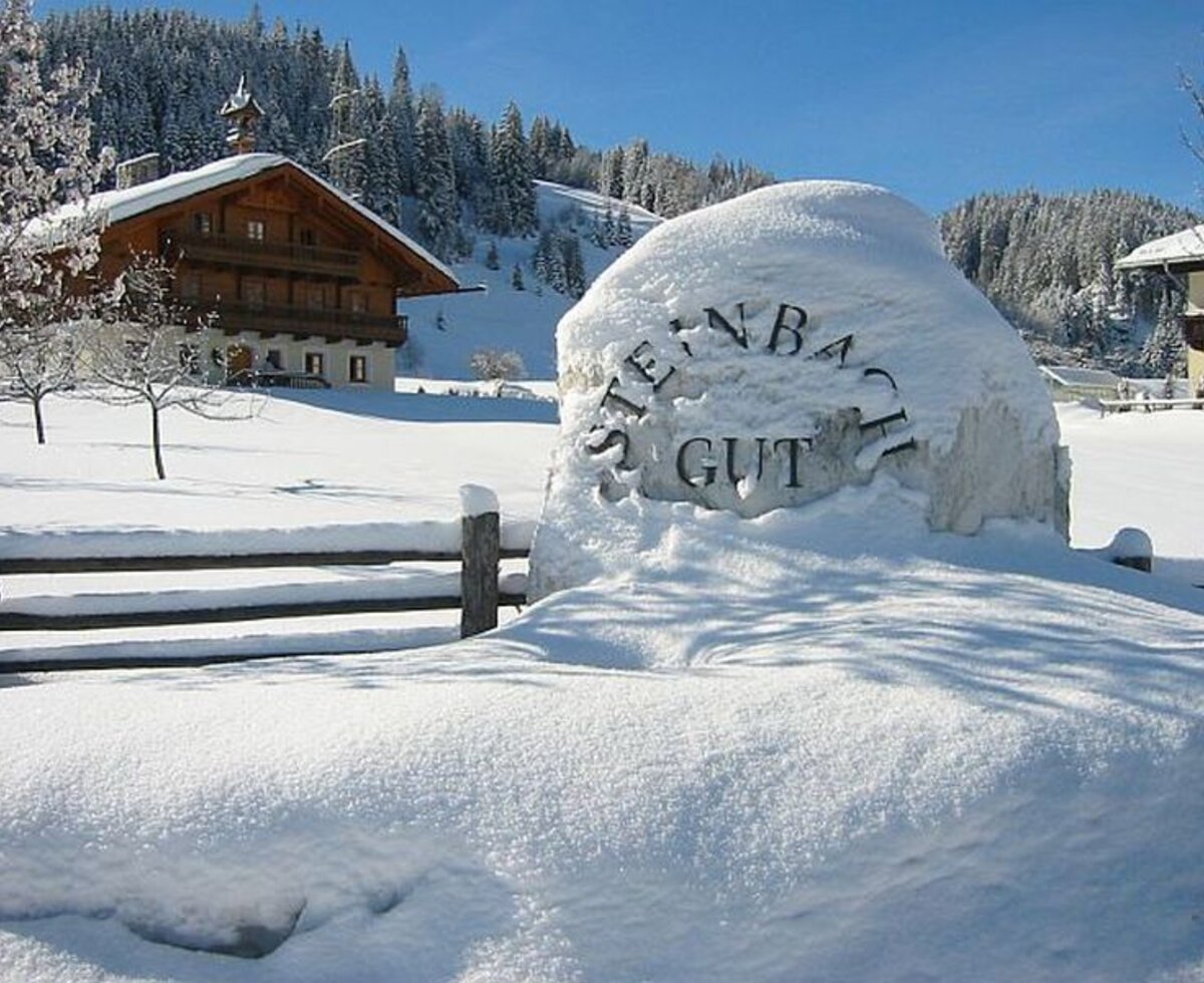 The Farm House in winter, surrounded by snow and featuring a stone sign with the property's name.