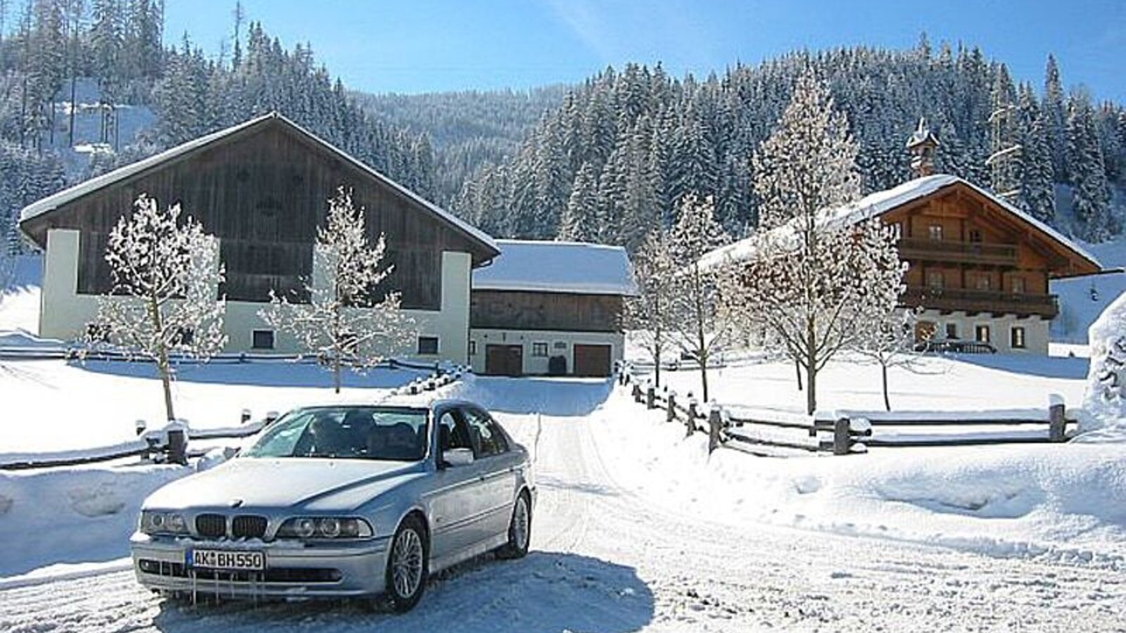 The Farm House complex during winter, featuring snow-covered buildings, a clear driveway, and a forested backdrop.