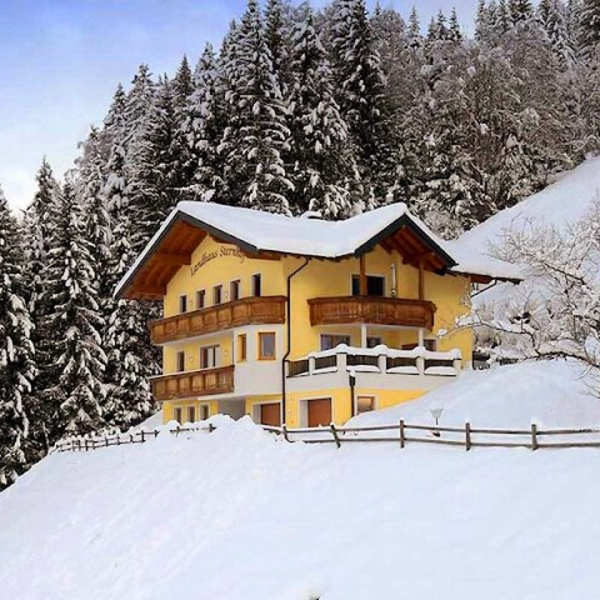 The yellow Farm House exterior, featuring wooden balconies and surrounded by snow-covered pine trees on a hillside.