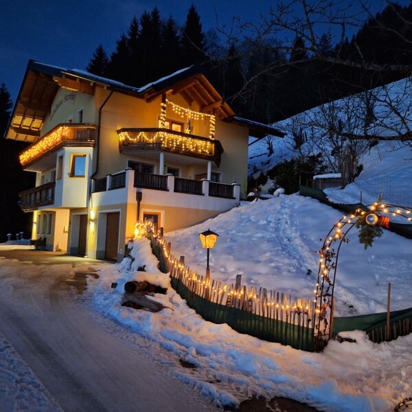 The farmhouse at night, festively lit and covered in snow.