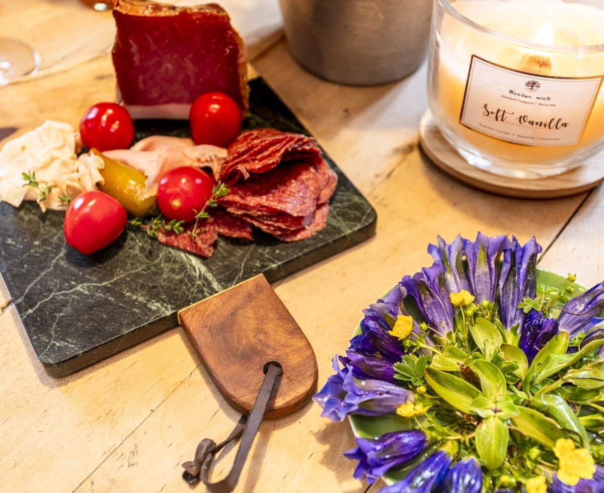 A platter with cold cuts, cheese, and vegetables, a lit candle, and a floral decoration as part of the offerings at the Bed and Breakfast.
