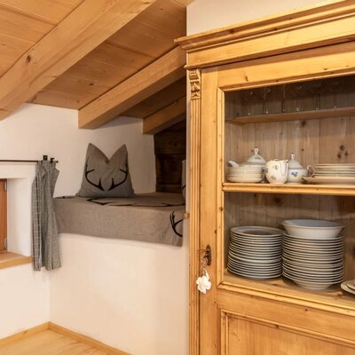 A wooden cabinet filled with dishes, a small window with checkered curtains, and a raised platform with a cushion.