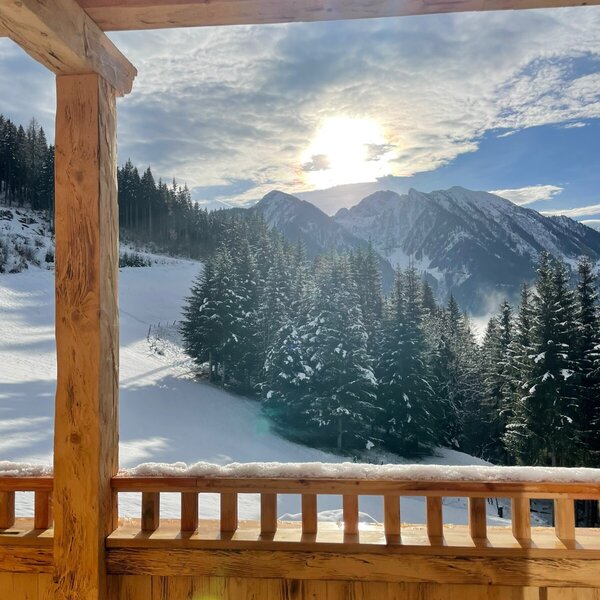 View from the farmhouse balcony showing the snowy mountain landscape and pine trees.