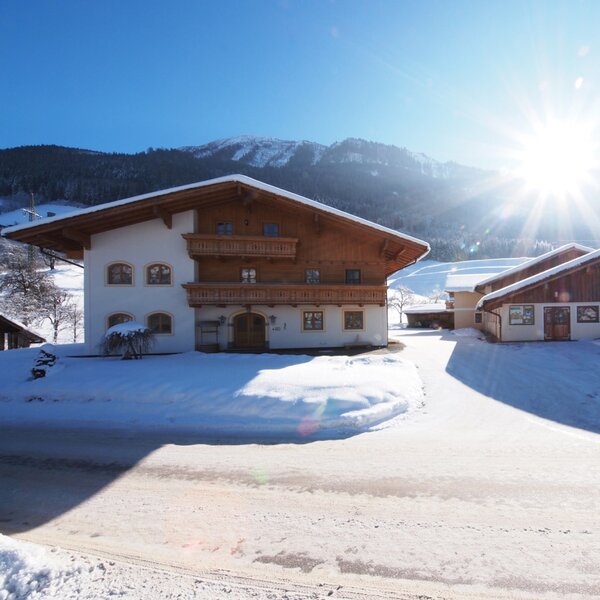 The snow-covered exterior of the Farm House property, featuring traditional buildings with balconies set against a backdrop of snowy mountains.