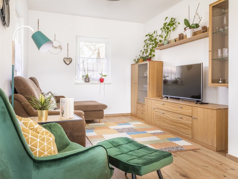 A cozy living area at our farm, featuring a comfortable brown sofa, a green armchair with an ottoman, a flat-screen TV, and charming decor, perfect for relaxing after a day of activities.