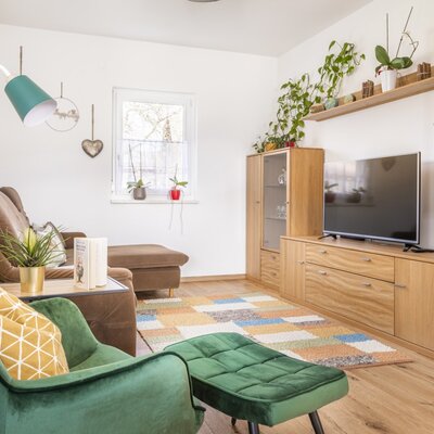 A cozy living area at our farm, featuring a comfortable brown sofa, a green armchair with an ottoman, a flat-screen TV, and charming decor, perfect for relaxing after a day of activities.