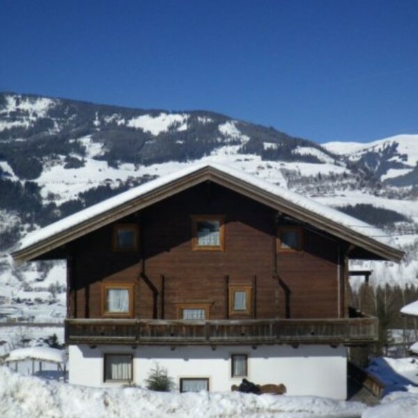 The farm house, featuring a wooden facade and a balcony, surrounded by a snow-covered landscape with mountain views.