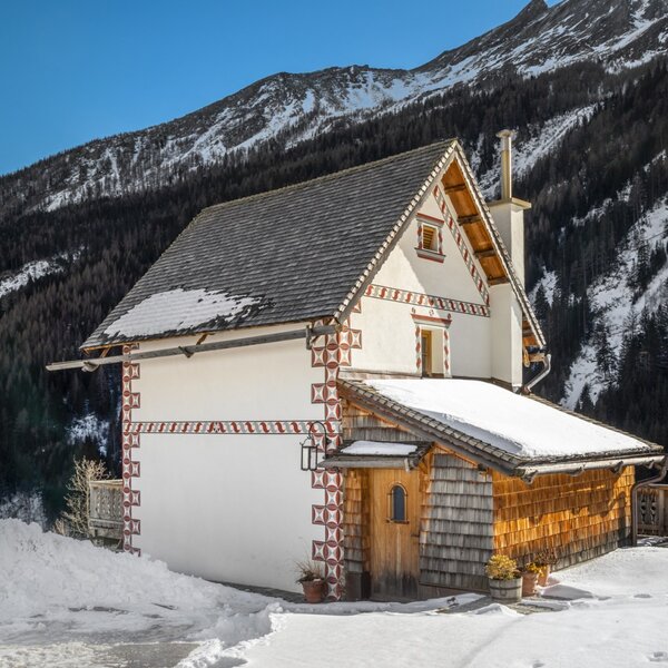 The farmhouse exterior features decorative wall patterns, a wooden entrance, and a snow-covered roof, set against a backdrop of snowy mountains.