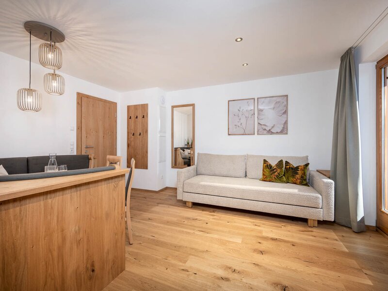Apartment living area with a sofa, dining table, and balcony access with mountain views.