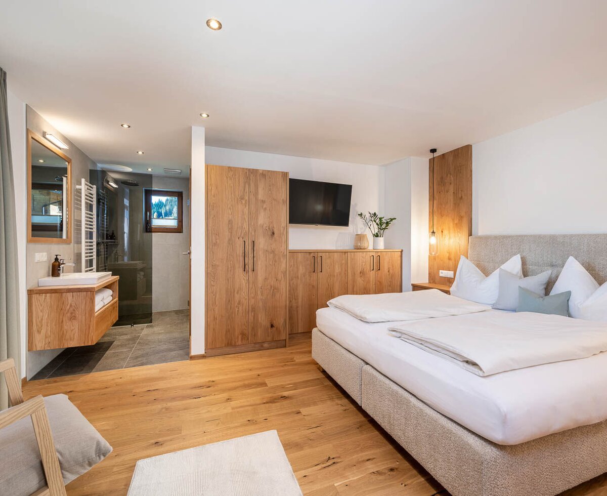 Bedroom in the apartment with a double bed, wooden furniture, television, and an open bathroom area with a shower.