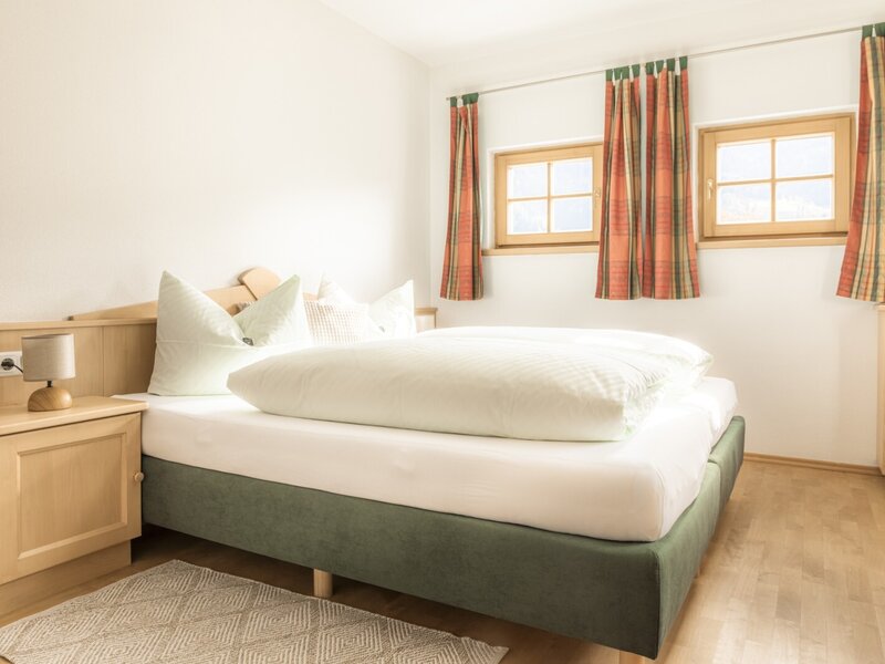 Double bedroom with a double bed, bedside table, and two windows.