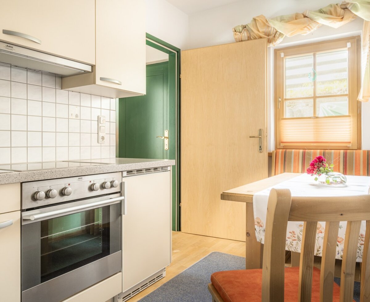 The kitchen, equipped with an oven, stovetop, and a dining area featuring a wooden table and bench by the window.