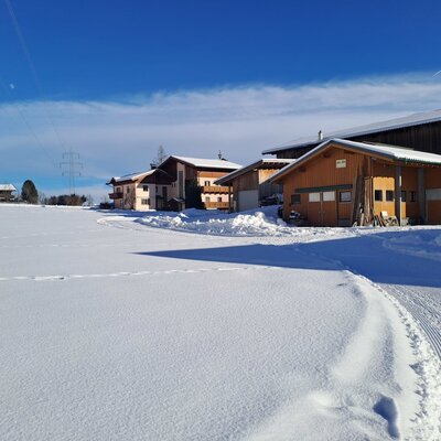 The Farm House property in a winter setting, featuring snow-covered buildings and fields under a clear blue sky.