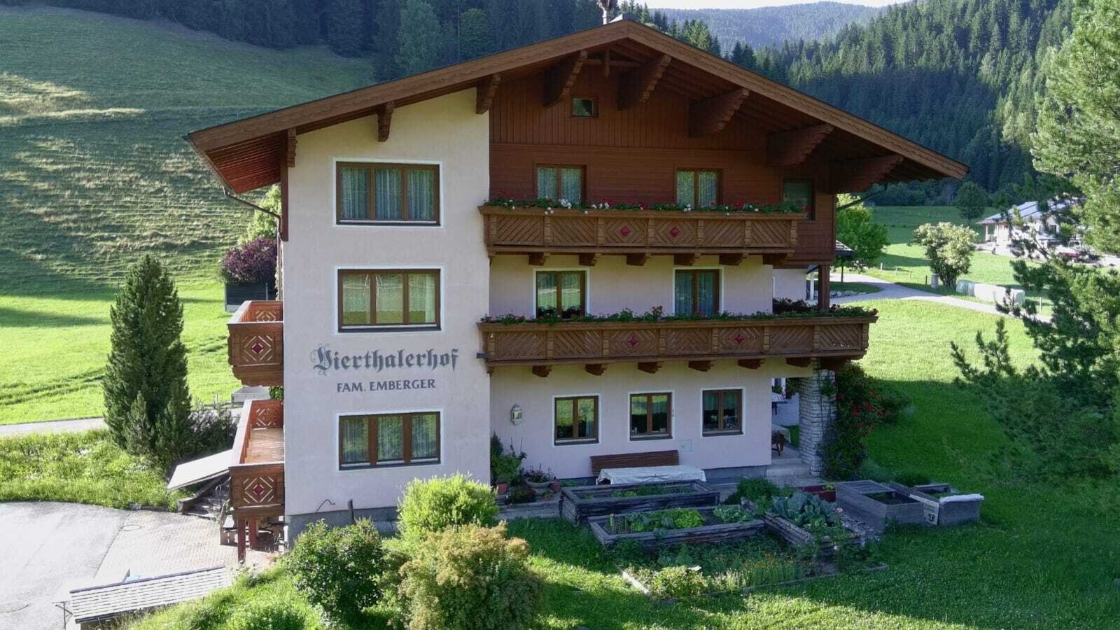 The Farm House exterior, featuring traditional wooden balconies adorned with flower boxes, surrounded by green hills.