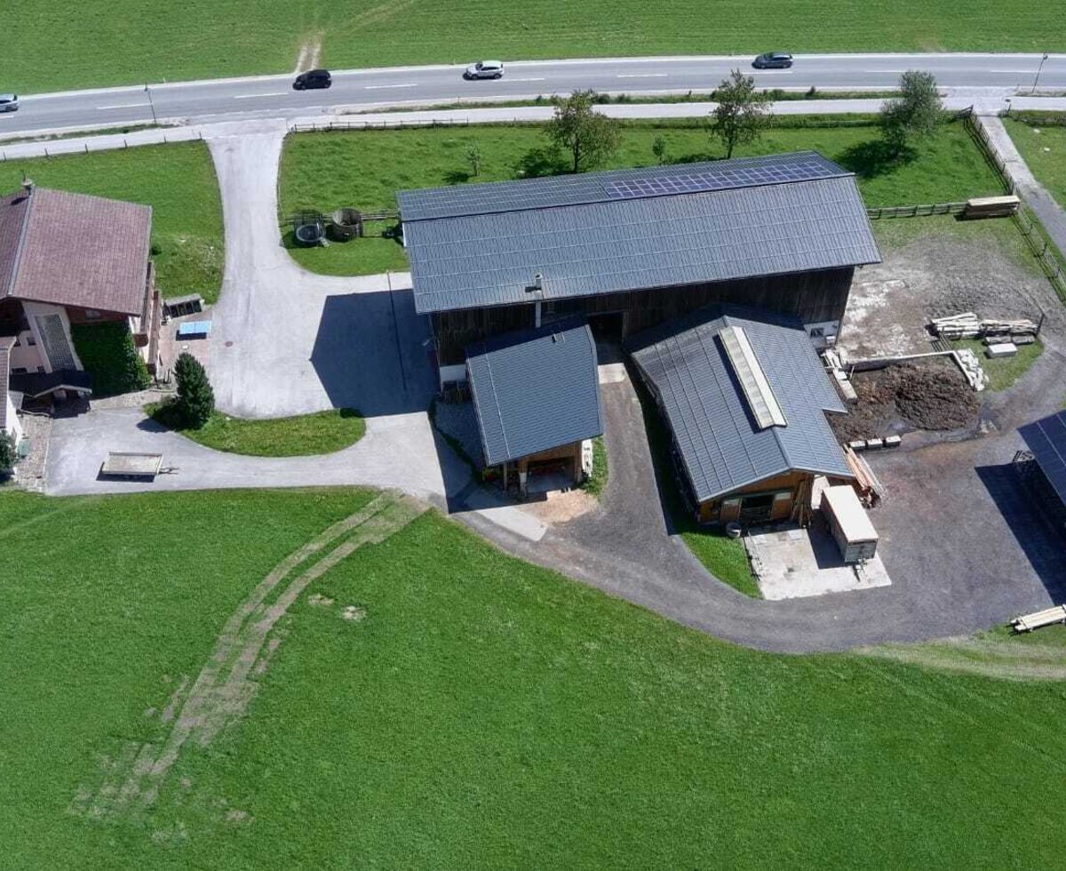 Aerial view of the farmhouse property, featuring its buildings, surrounding green fields, and the access road.