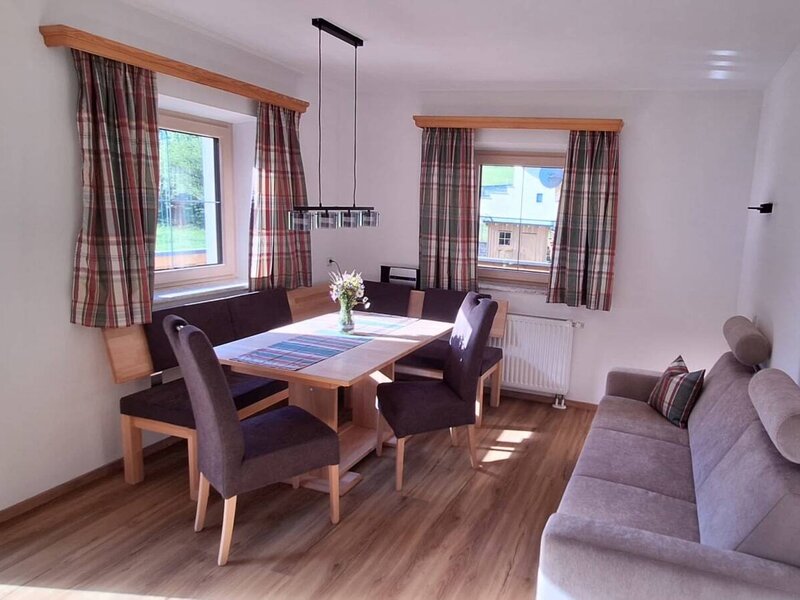 Living and dining area of the Ferienwohnung, equipped with a wooden dining table, corner bench, chairs, and a sofa.
