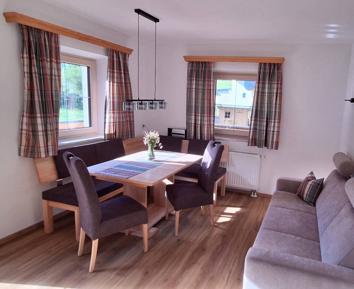 Living and dining area of the Ferienwohnung, equipped with a wooden dining table, corner bench, chairs, and a sofa.
