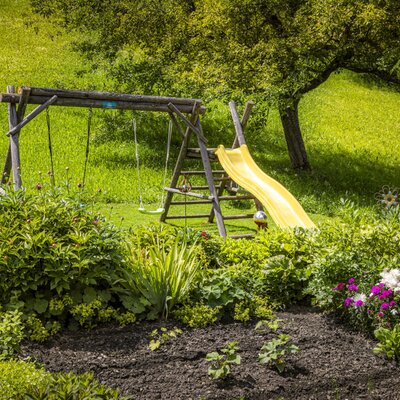 The Ferienwohnung's lush garden featuring a beautifully planted flower bed and a wooden playground with a slide and swing.