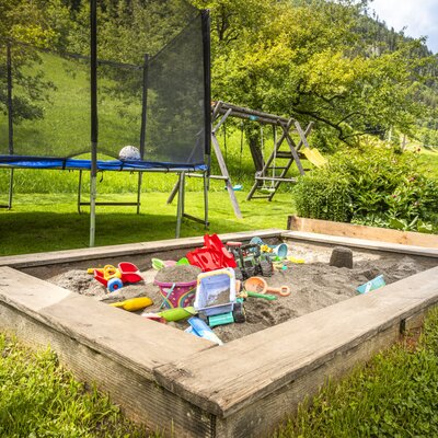 The Ferienwohnung's inviting garden, featuring a lively children's play area with a sandbox, trampoline, and swing set.