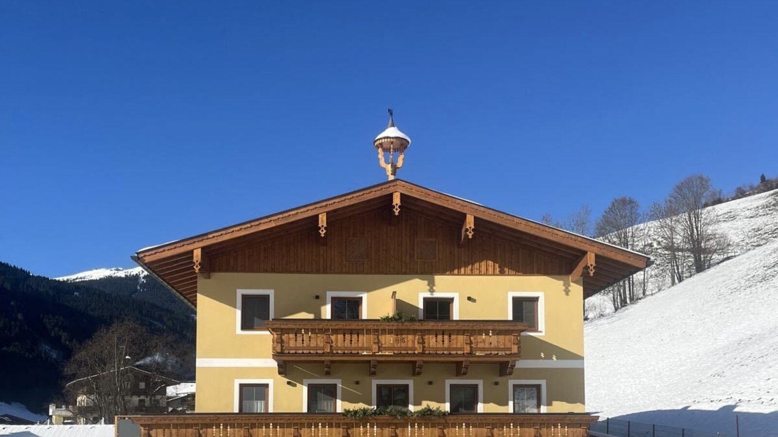 Exterior view of the farmhouse with a yellow facade, wooden balconies, and a snow-covered landscape.
