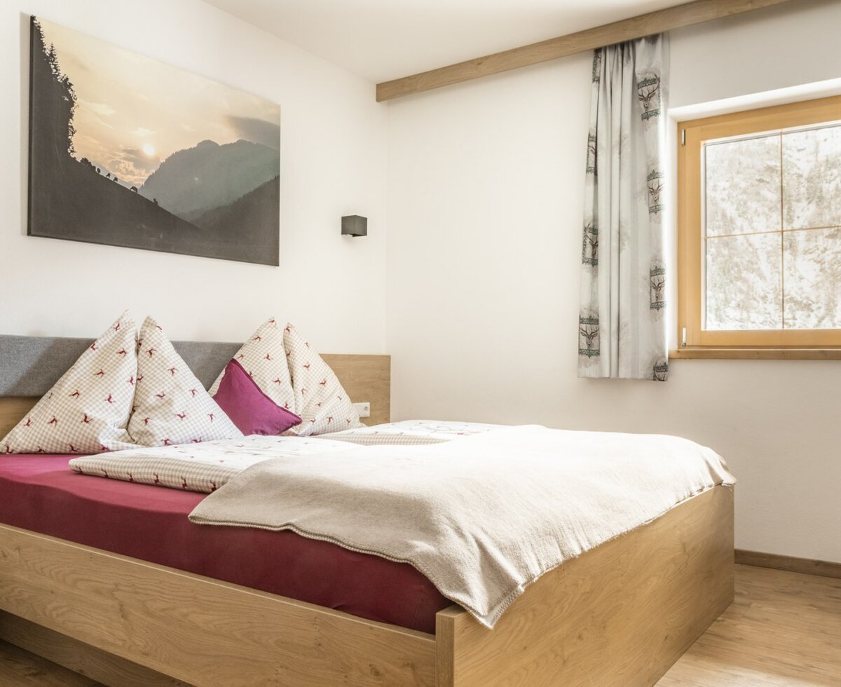 Bedroomm with a double bed, nightstand, and window with curtains.