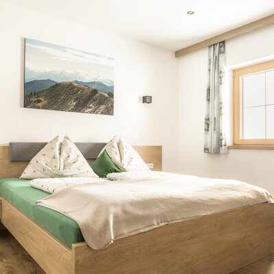 Double bedroom with a wooden bed, nightstand, and window with curtains.