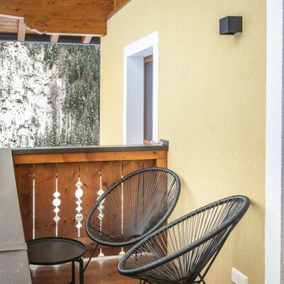 Balcony of the farmhouse with two chairs, a table, and a view of snow-covered trees.