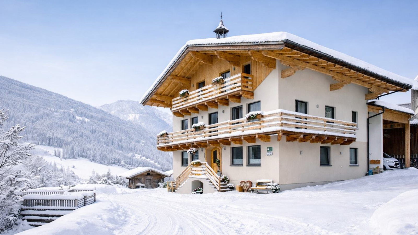 The snow-covered farmhouse with wooden balconies and a view of the winter mountain landscape.