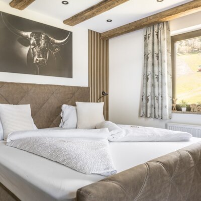 Bedroom of the Ferienwohnung with a double bed, large bull artwork, wooden ceiling beams, and a window offering a green landscape view.