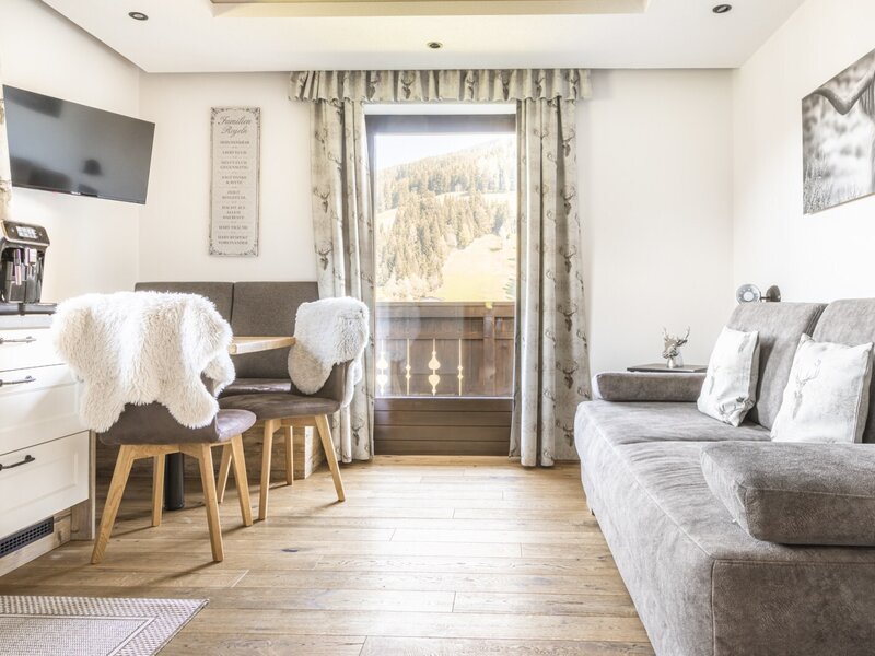 Living area of the holiday apartment with a sofa, dining area, kitchenette, TV, and balcony access with mountain views.
