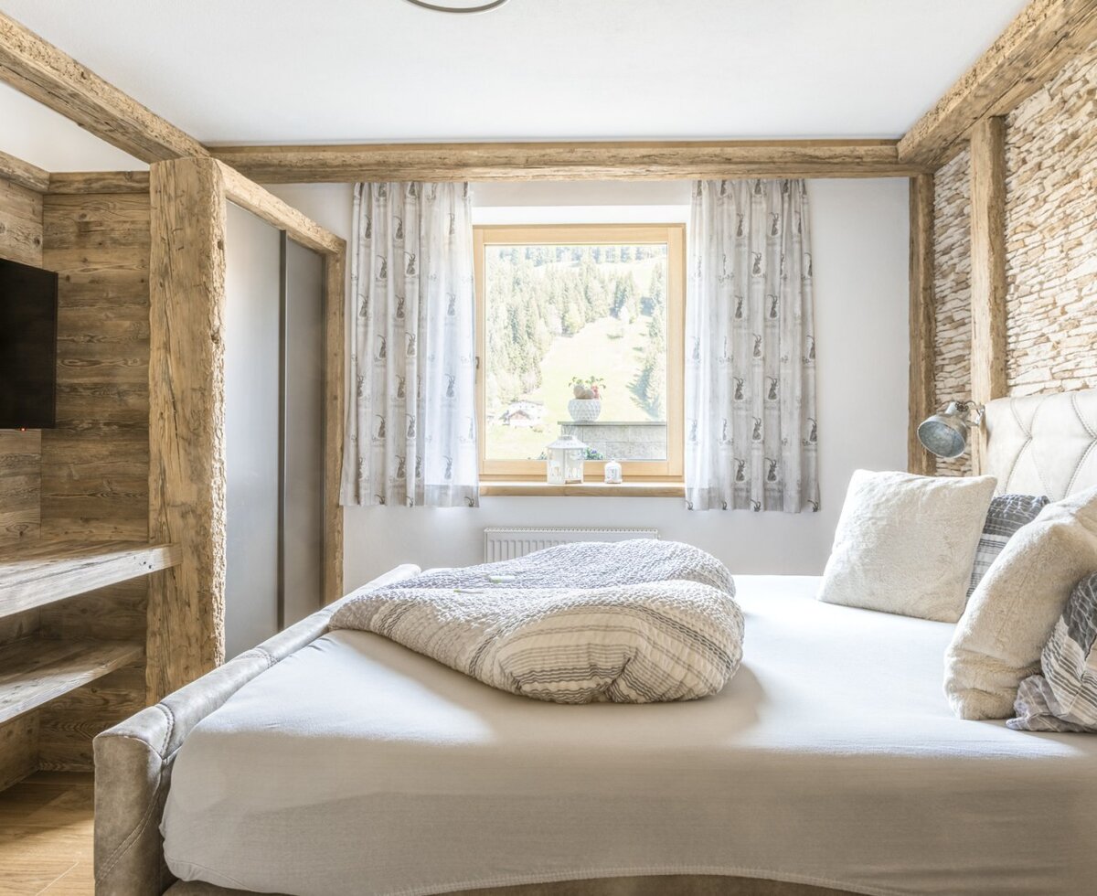 Bedroom in the Ferienwohnung featuring a double bed, wooden beams, a stone accent wall, a built-in TV, and a window with a mountain view.