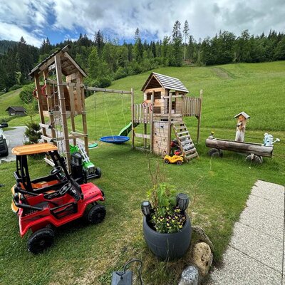 The children's playground at the Ferienwohnung features wooden play equipment, swings, a slide, and a playhouse.