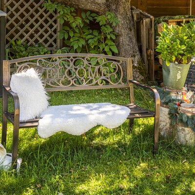 An inviting metal bench with cozy faux fur throws in the apartment's green garden.