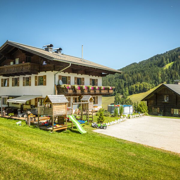 The charming apartment house featuring a spacious, sunny garden with a children's play area, surrounded by scenic green hills.
